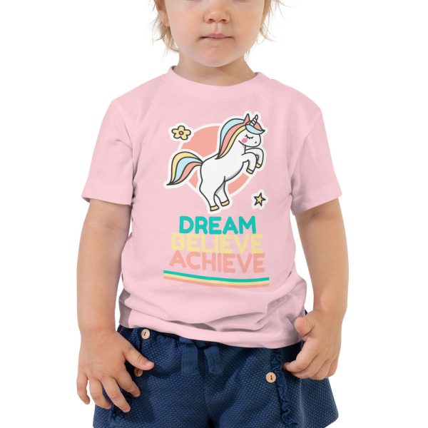 A toddler wearing a pink 'Dream Believe Achieve' Unicorn T-shirt.