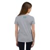 The back view of a girl wearing a Youth Love, Waves & Mermaids T-Shirt, standing near crashing waves.